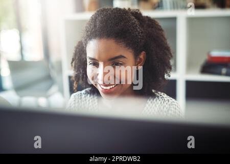 Sie macht alles mit einem Lächeln auf ihrem Gesicht. Eine junge Geschäftsfrau, die an ihrem Schreibtisch am Computer arbeitet. Stockfoto