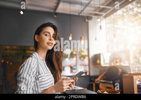 Mit diesem Tablet läuft alles reibungslos. Abgeschnittenes Porträt einer attraktiven jungen Frau, die an einem digitalen Tablet arbeitet, während sie in ihrem Café steht. Stockfoto