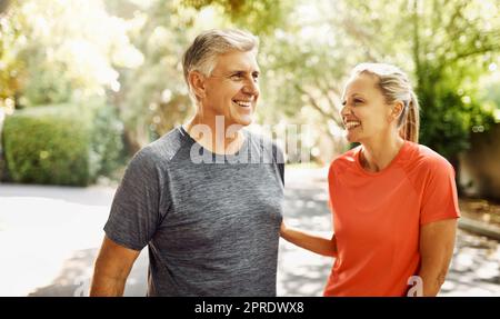 Glückliches, reifes Paar, das aktiv, fit und gesund bleibt, während es in der Natur joggt, joggt oder spaziert. Lachender älterer Mann und lachende Frau, die eine Pause vom Training oder Training genießen Stockfoto