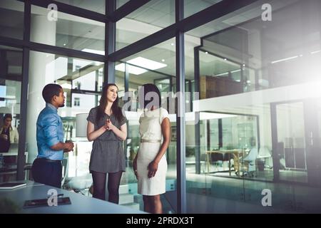 Das Business-Team steht und spricht im Büro zusammen. Besprechung und offenes Gespräch mit Kollegen am Arbeitsplatz. Coaching und Unterstützung neuer Mitarbeiter im Unternehmen als Mentor des Unternehmens. Stockfoto