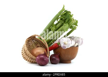 Rote und gelbe Zwiebeln im Korbkorb, Knoblauchzwiebeln und Nelken in Holzschüssel, roter Chilischote und Sellerie auf weißem Hintergrund Stockfoto