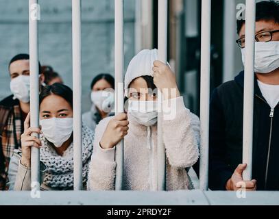 Fremde in Isolation tragen covid Gesichtsmaske an der Grenze oder in Quarantäne oder Flughafen sehen unglücklich, aufgebracht und wütend aus. Arme Flüchtlinge, Einwanderer und Touristen, die hinter einem abgeschlossenen Tor festsitzen Stockfoto