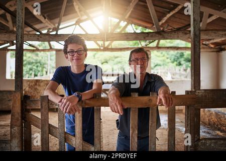 Der Familienbetrieb. Ein reifer Bauer und sein junger Sohn stehen in einer Scheune auf dem Familienhof. Stockfoto