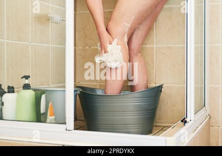 Es gibt einfache Möglichkeiten, Wasser zu sparen. Eine unkenntliche Frau wäscht in einem Eimer, der zu Hause in die Dusche gestellt wurde. Stockfoto