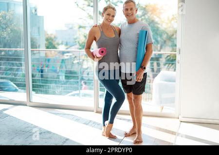 Der einzige Weg, vorwärts zu kommen, ist gemeinsam. Ganzkörperportrait eines liebevollen reifen Paares, das mit seinen Yogamatten zu Hause steht. Stockfoto