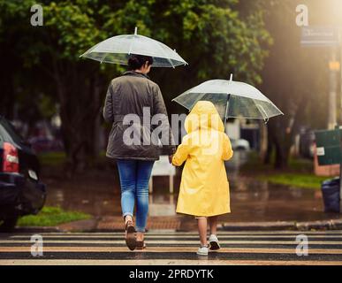 Auf unserem Weg, durch den Regen gehen wir. Rückansicht eines nicht erkennbaren kleinen Jungen und seiner Mutter, die die Hände hielt und draußen im Regen ging. Stockfoto