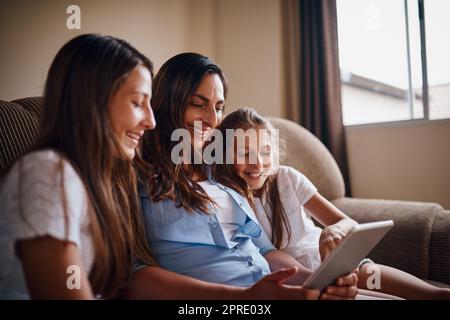 Eine attraktive Mutter, die sich mit ihren beiden Töchtern zu Hause Filme auf einem Tablet ansieht. Stockfoto