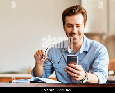 Ohne seine digitalen Verbindungen kann nichts getan werden. Ein junger Mann, der zu Hause ein Handy benutzt. Stockfoto