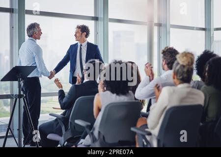 Sie haben es sich verdient. Zwei Geschäftsleute schütteln sich während eines Seminars im Konferenzraum die Hände. Stockfoto