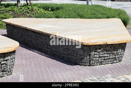 Holzbänke aus Gabionenkörben mit Steinen im Inneren. Holz auf Gabionen montiert. Bänke in modernem Design. Detaildarstellung einer flachen Gabionenwand mit Holzplatte zur Verwendung als Bank. Stockfoto