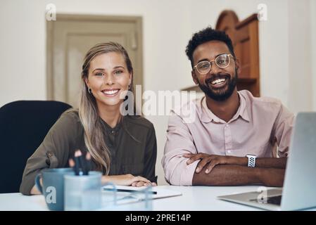 Zufriedene, vielfältige Mitarbeiter, die gemeinsam an einem Projekt arbeiten, sitzen an einem Bürotisch und sind mit der Partnerschaft zufrieden. Porträt von jungen Kollegen mit positiver Einstellung, die über das Geschäftswachstum lächeln Stockfoto