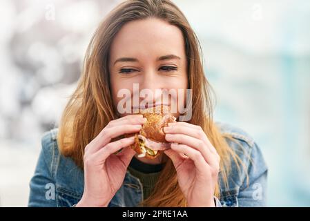 Schneller Snack, dann wieder zum Spaß. Porträt einer schönen jungen Frau, die draußen in einem Vergnügungspark ein Sandwich isst. Stockfoto