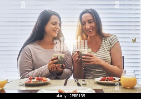 Sich morgens zum Lachen bringen. Zwei junge Frauen, die morgens zu Hause zusammen frühstücken. Stockfoto