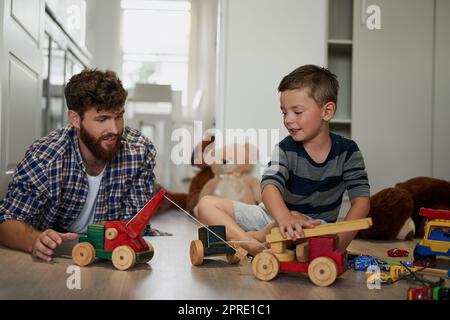 Wie ein Vater, wie ein Sohn. Ein hübscher junger Mann und sein Sohn spielen mit Spielzeug auf dem Schlafzimmerboden. Stockfoto