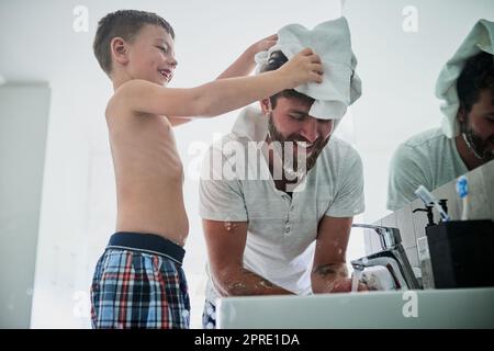 Ich helfe Euch, Papa. Ein kleiner Junge, der seinen Vater beim Rasieren im Badezimmer zu Hause abwischt. Stockfoto