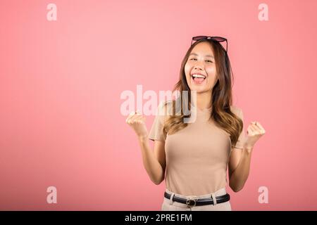 Eine junge Frau, die eine Brille trägt, hebt die Hand hoch und feiert ihre erfolgreiche Geste Stockfoto