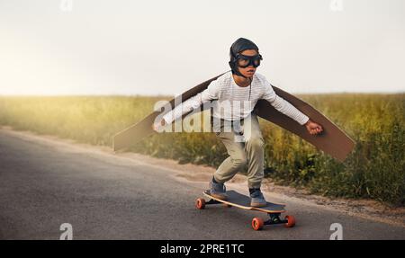 Haben Sie gesehen, ein Kind jeder Kühler. Ein kleiner Junge vorgibt, mit einem Paar von Pappe Flügel fliegen, während ein Skateboard draußen reiten. Stockfoto