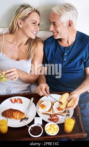 Ich kann mir keinen besseren Start in den Tag vorstellen. Ein liebevolles reifes Paar genießt das Frühstück im Bett zu Hause. Stockfoto