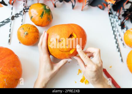 Halloween am 31. Oktober. Der Schritt-für-Schritt-Prozess des Schnitzens eines Kürbisses. Das Mädchen schneidet das Gesicht des Kürbisses mit einem Messer. Blick von oben Stockfoto