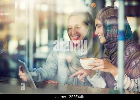 Technologie verbindet online und im echten Leben. Zwei Frauen nutzen ein digitales Tablet zusammen in einem Café. Stockfoto