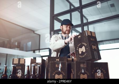 Ein Paket, das für eine glückliche Person geliefert wird. Ein fröhlicher junger Mann packe tagsüber Kartons übereinander in einem Bürogebäude. Stockfoto