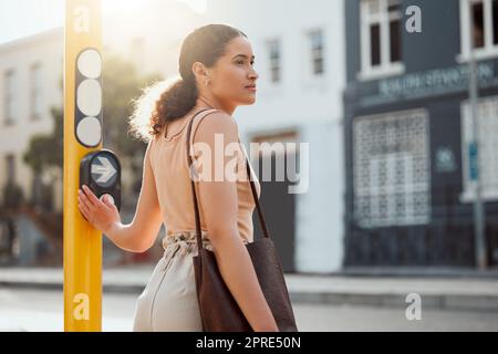 Attraktive weibliche Fußgängerin, die bereit ist, die Straße zu überqueren, auf grünes Licht wartet und den Knopf bei einer Frau drückt, die eine junge Stadt kreuzt, auf einem Morgenspaziergang zur Arbeit, steht und schaut auf den Verkehr. Stockfoto