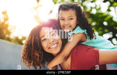 Die beste Zeit ist Mama und ich Zeit. Ein glückliches kleines Mädchen und ihre Mutter genießen eine Huckepack Fahrt in ihrem Hinterhof. Stockfoto