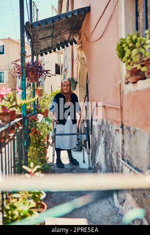 Das ist seit vielen Jahren mein Zuhause. Porträt einer älteren Frau, die auf ihrer Vorhalle in einer alten Stadt steht. Stockfoto