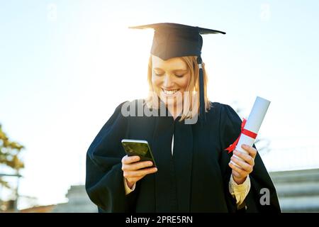 Der schnellste Weg, um allen von ihrem großen Tag zu erzählen. Studentin benutzt ihr Handy am Abschlusstag. Stockfoto
