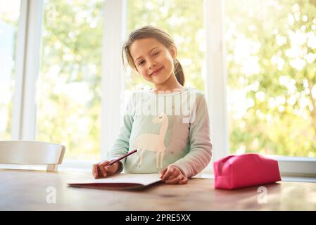 Ich liebe Malbücher. Porträt eines fokussierten kleinen Mädchens, das Bilder in einem Buch zeichnet, während es zu Hause auf die Kamera schaut. Stockfoto