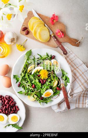 Löwenzahnsalat mit Eiern, Kartoffeln und Bohnen auf hellen Tischhintergrund Stockfoto