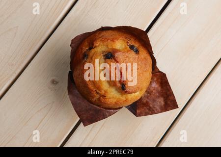 Blick von oben auf frischen Muffin mit Schokoladenstückchen in Papierverpackung auf einem Holztisch Stockfoto