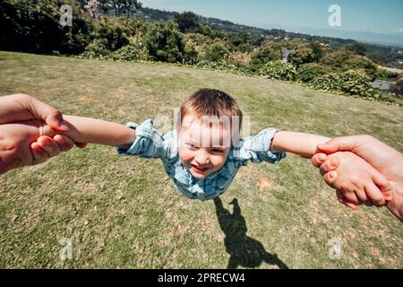 Nahaufnahme des kleinen Jungen, der von den Eltern draußen in der Natur herumgeschwenkt wird. POV Aufnahme eines kleinen Jungen, der vorgibt zu fliegen und Spaß während des Vaters zu haben Stockfoto