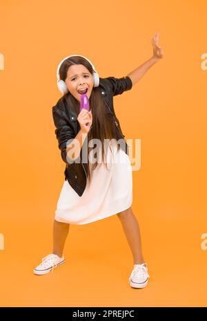 Online Karaoke singen. Musik in kabellosen Ohrhörern. Kind verwenden Kamm als Mikrofon. Kind hören Musik im Headset. Kleines Mädchen genießen DJ-Musik. Glücklich Stockfoto