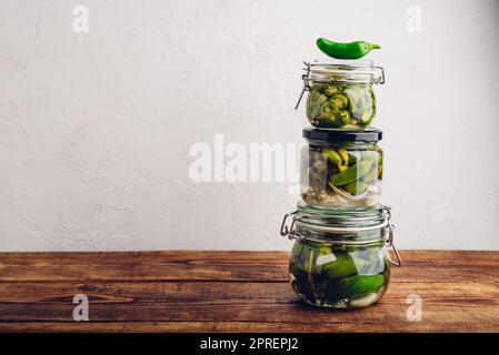 Drei Glas Jalapeno Peppers aus der frischen Dose mit Kräutern und Knoblauch auf einem Holztisch. Speicherplatz Kopieren Stockfoto