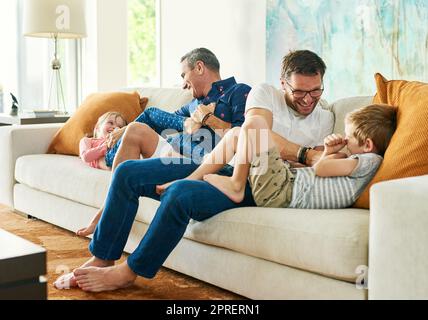 Erhalten ihre tägliche Dosis von Kitzeln. Ganzkörperaufnahme einer liebevollen vierköpfigen Familie auf dem Sofa zu Hause. Stockfoto