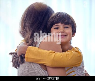 Mama nennt mich ihren kleinen Mann. Ein entzückender kleiner Junge umarmt seine Mutter zu Hause liebevoll. Stockfoto