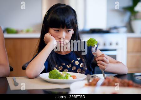 Warum werde ich wieder gefüttert. Ein kleines Mädchen weigert sich, ihren Brokkoli zu essen. Stockfoto