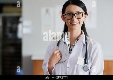 Sie begrüßt alle ihre Patienten mit einem freundlichen Lächeln. Beschnittenes Porträt einer jungen Ärztin, die in ihrem Büro im Krankenhaus steht. Stockfoto