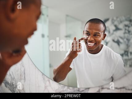 Ein hübscher junger Mann, der im Badezimmer zu Hause Feuchtigkeitscreme auf sein Gesicht aufbringt, bringt seine Hautpflegeroutine auf die nächste Stufe. Stockfoto