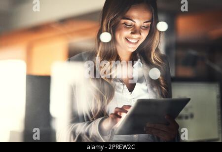 Überstunden, Überstunden und Hingabe mit einer glücklichen, positiven und motivierten Geschäftsfrau, die in ihrem Büro an einem Tablet arbeitet. Junge weibliche Führungskraft, die lächelt und sich engagiert und entschlossen fühlt Stockfoto