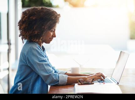 Shes immer hart bei der Arbeit. Eine attraktive junge Frau, die zu Hause an ihrem Laptop arbeitet. Stockfoto