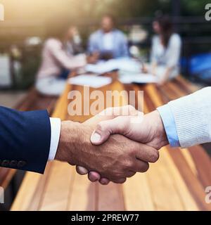 Und der Deal wurde besiegelt. Nahaufnahme von zwei nicht erkennbaren Geschäftsleuten, die sich im Hintergrund mit ihren Kollegen die Hände schüttelten. Stockfoto