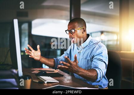 Was meinen Sie mit Fehler? Ein junger Geschäftsmann, der wütend auf den Computer schaut, während er spät abends bei der Arbeit arbeitet. Stockfoto