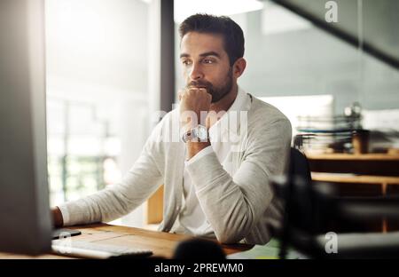 Ein hübscher junger Geschäftsmann, der spät an einem Computer in einem Büro arbeitet. Stockfoto