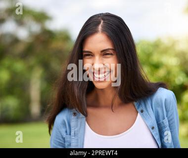 Sie lächelt, weil sie glücklich ist. Eine attraktive junge Frau, die draußen steht. Stockfoto