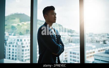 Dieses Jahr würde größer und besser werden. Ein junger Geschäftsmann, der nachdenklich aus einem Bürofenster schaut. Stockfoto