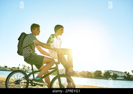 Brüder auf einem Fahrrad. Ein kleiner Junge, der seinem jüngeren Bruder einen Aufzug auf einem Fahrrad draußen gab. Stockfoto