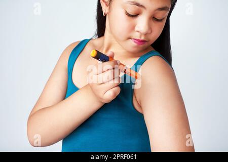 Ihr Diabetes unter Kontrolle zu halten. Studioaufnahme eines niedlichen jungen Mädchens, das sich mit Insulin injiziert, vor grauem Hintergrund. Stockfoto