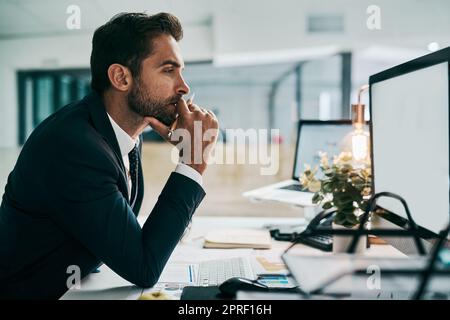 Ich werde sicherstellen, dass ich diese Arbeit richtig erledigt habe. Ein fokussierter junger Geschäftsmann, der einen Computerbildschirm betrachtet, während er im Büro nachdenkt. Stockfoto